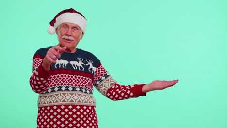 Grandfather-in-Christmas-deer-sweater-showing-thumbs-up-and-pointing-at-on-blank-advertisement-space