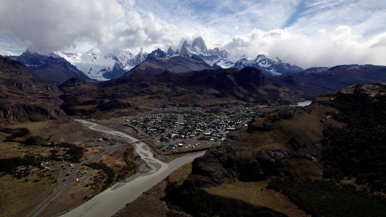 Un piccolo paese è annidato in una valle, circondato da montagne imponenti e un fiume sinuoso. Di giorno, il cielo arricchisce il paesaggio della Patagonia.
