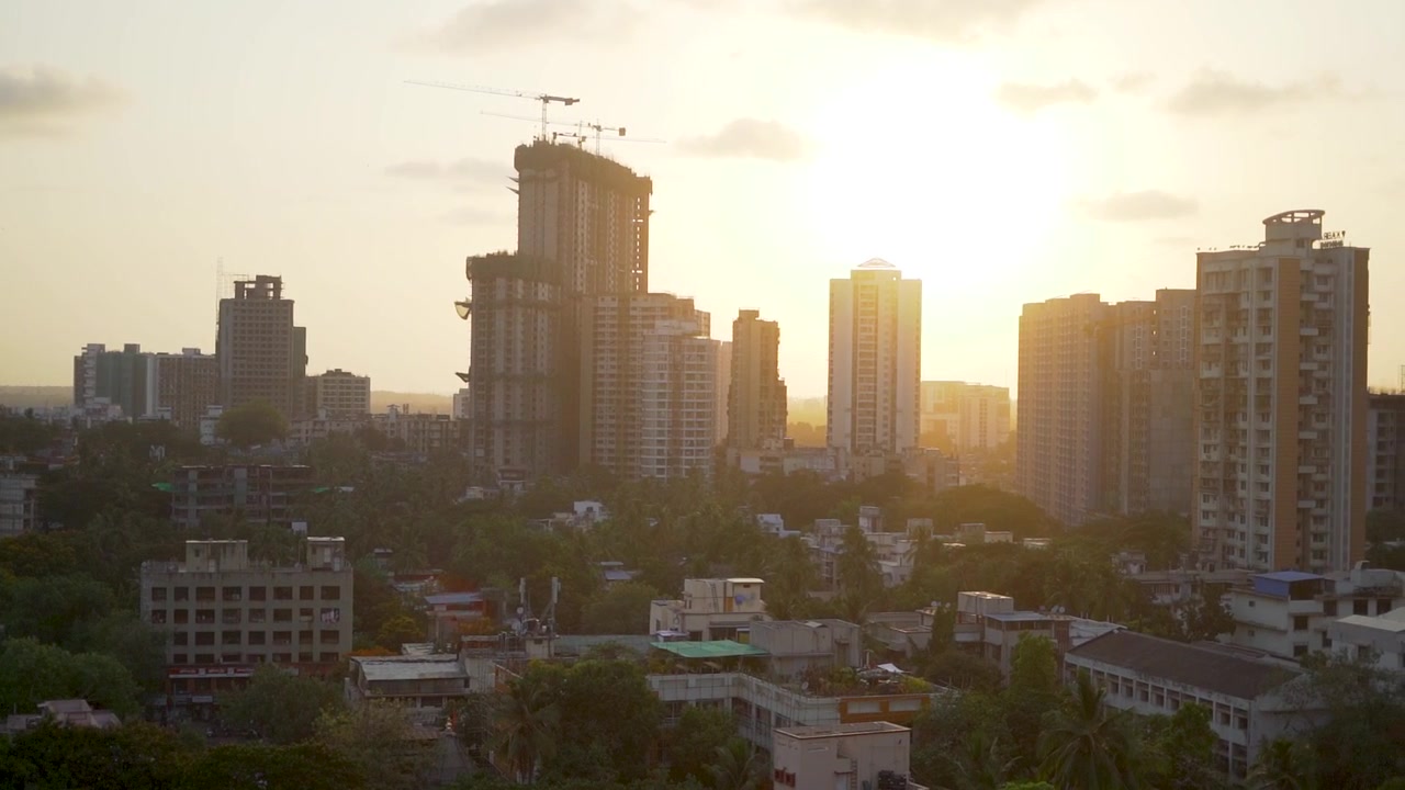 Horizonte de Mumbai iluminado pela luz dourada e quente do sol, mostrando edifícios residenciais altos, atividade de construção e desenvolvimento urbano denso durante o pôr do sol