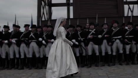 woman in 18th century dress facing military