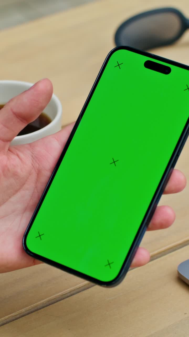 Persona che tiene uno smartphone con uno schermo verde su un tavolo di legno