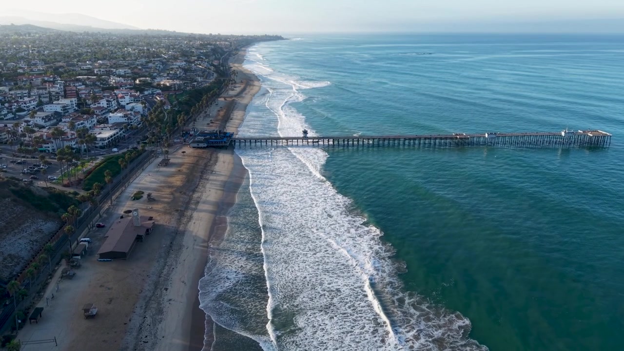 Una vista mozzafiato del molo di San Clemente e della costa della California mentre il drone scivola dolcemente lungo la riva da un'alta quota. Le onde del Pacifico si infrangono contro la riva in questo scatto mozzafiato