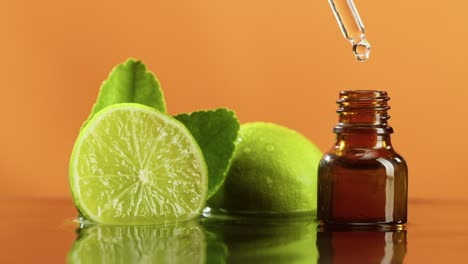 dripping oil from pipette into bottle close-up, lime juice. making aroma serum on orange background. dropping liquid citrus extract, skincare routine, treatment spa concept. traditional medicine