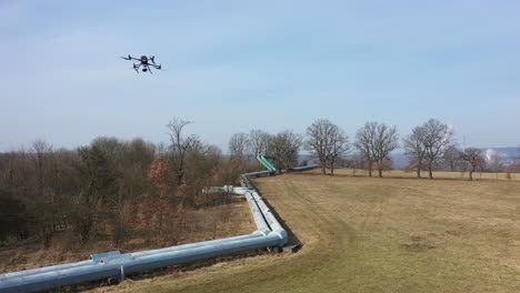 quadcopter drone aircraft flying above pipelines and meadow on sunny day, aerial tracking view