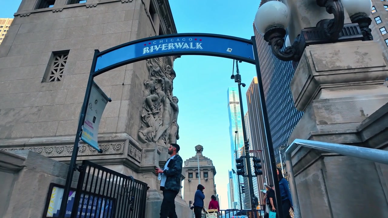 Chicago, USA, 7 maggio 2026: Arco d'ingresso del Chicago Riverwalk con sculture in pietra e lampioni. Angolazione bassa di un cartello blu incorniciato da una torre di ponte classica, luci a globo e rilievi intagliati
