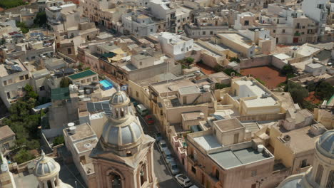 Bonita-Iglesia-Azul-Y-Beige-En-Una-Pequeña-Ciudad-Mediterránea-En-La-Isla-De-Malta,-Inclinación-Aérea-Hacia-Abajo-A-La-Luz-Del-Atardecer