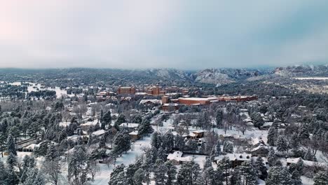 Paralaje-Aéreo-Panorámico-Sobre-Un-Bosque-Siempre-Verde-Cubierto-De-Nieve-Mientras-El-Sorprendente-Hotel-Marrón-Se-Destaca-En-Las-Montañas-Rocosas