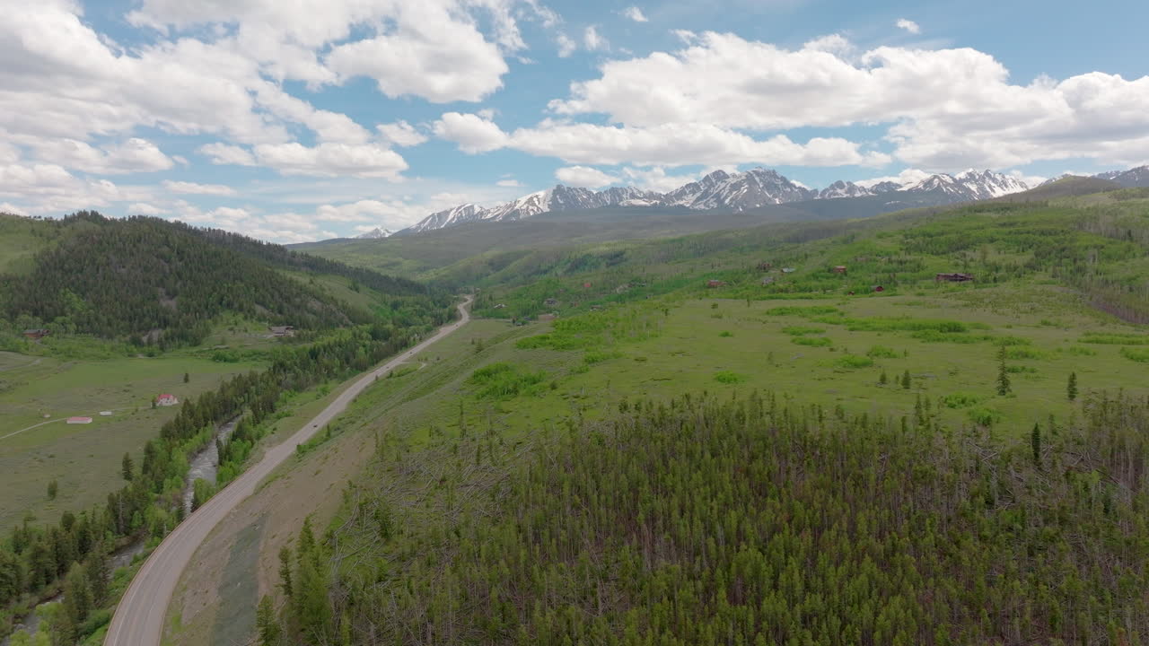 vista aérea del hermoso desierto de colorado y la cordillera con picos cubiertos de nieve en un día soleado de cielo azul en el verano con campos verdes, árboles y casas de montaña