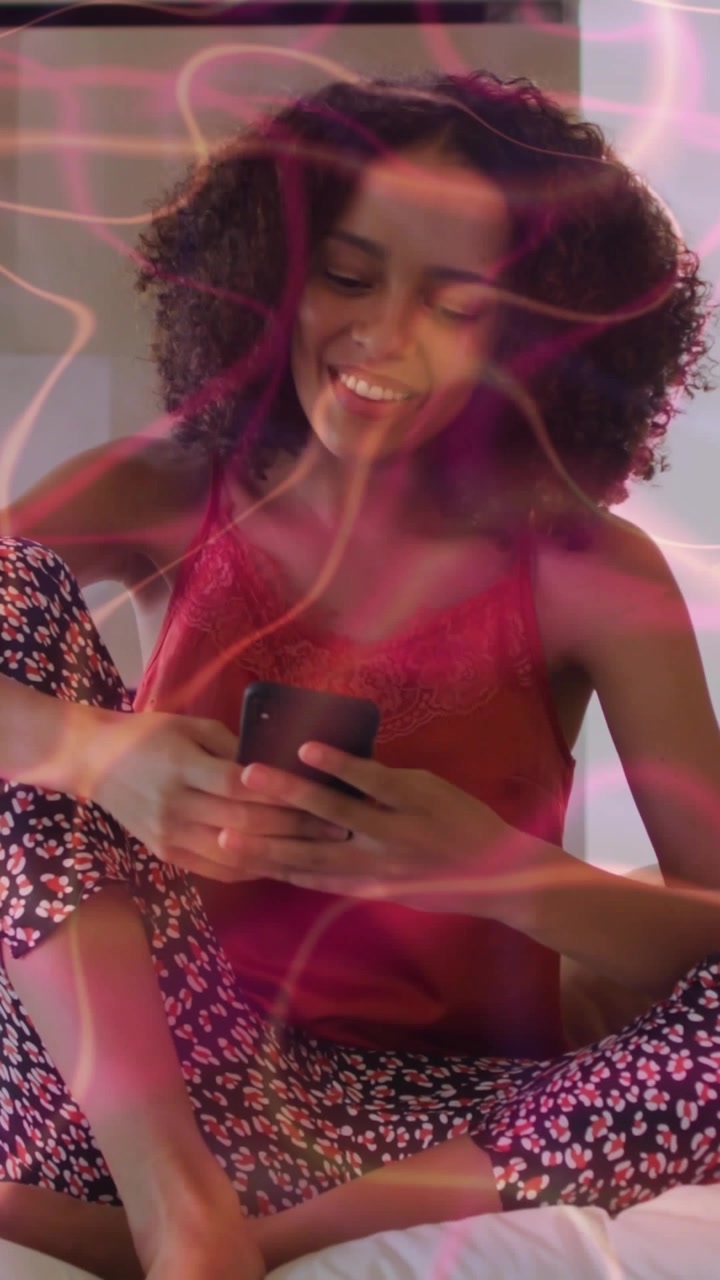 Video verticale: Donna che usa il telefono, reagendo ai messaggi a letto, con una sovrapposizione rosa che le scivola sul viso