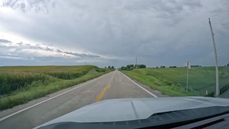 pov - driving on a country road past alfalfa and corn fields on a cloudy, rainy day in late summer in the midwest