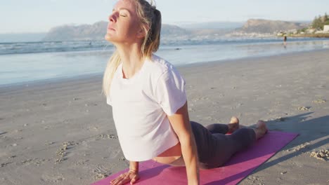 Mujer-Caucásica-Practicando-Yoga,-Estirándose-En-La-Playa.