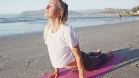 caucasian woman practicing yoga, stretching at the beach