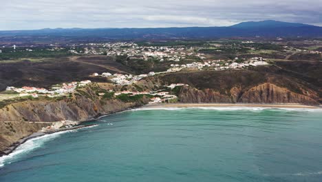 Playa-De-Praia-Da-Arrifana-En-El-Oeste-De-Portugal-Con-La-Ciudad-De-Picao-En-La-Parte-Superior-Del-Terreno,-Toma-Panorámica-Aérea-A-La-Derecha