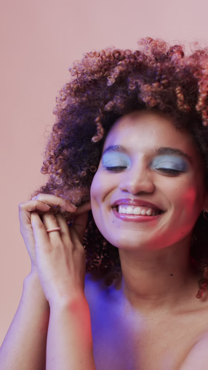 Vídeo vertical de mulher birracial com cabelo escuro em luz azul e rosa, em câmera lenta.