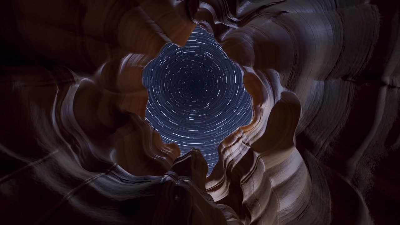 Looking up from inside a narrow sandstone canyon toward a circular opening in the night sky, with visible star trails and warm rock walls creating a dramatic