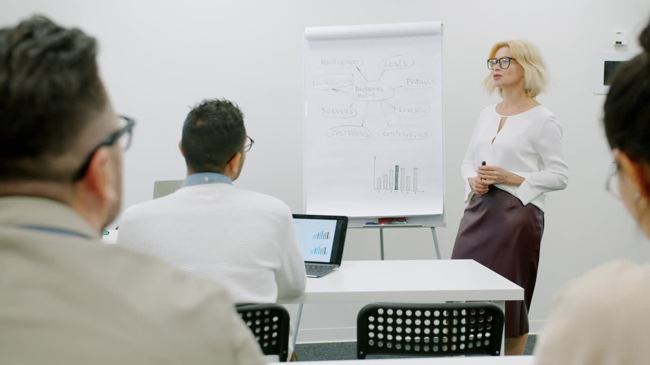 Businesswoman speaking in boardroom making presentation pointing at charts talking to people