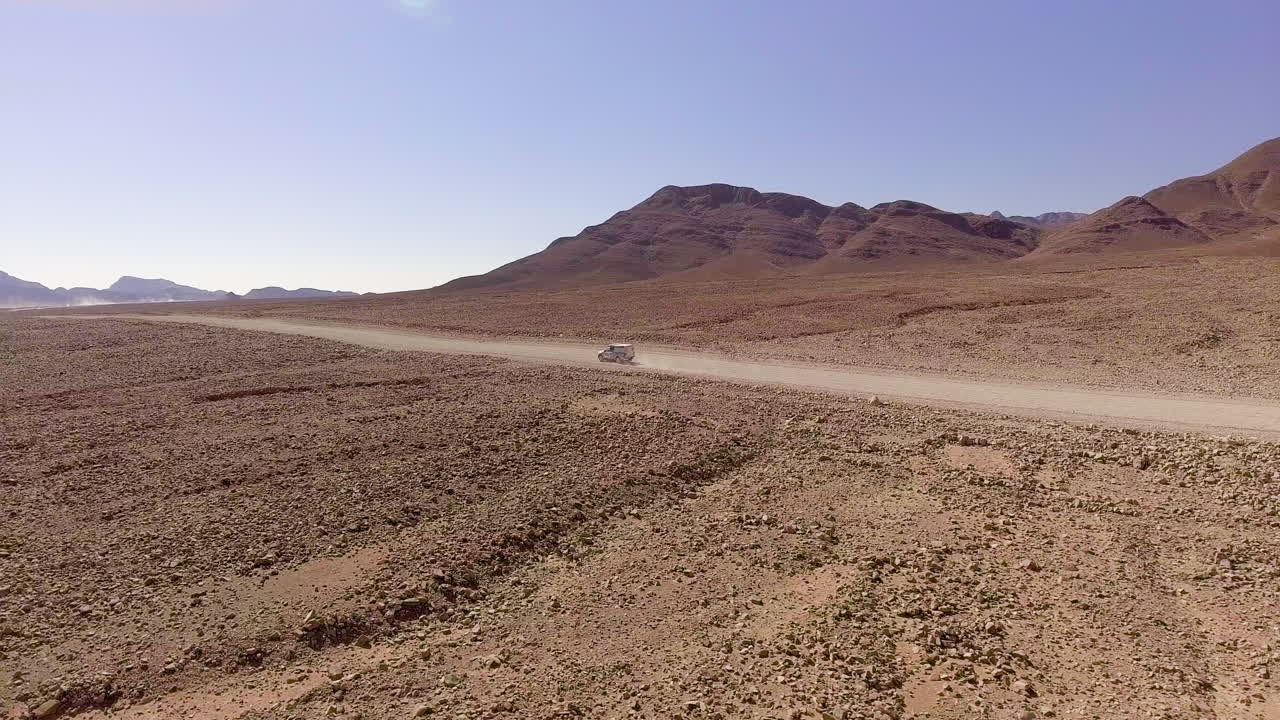 Aerial Pan, car driving through rugged desert landscape in Namibia, Africa