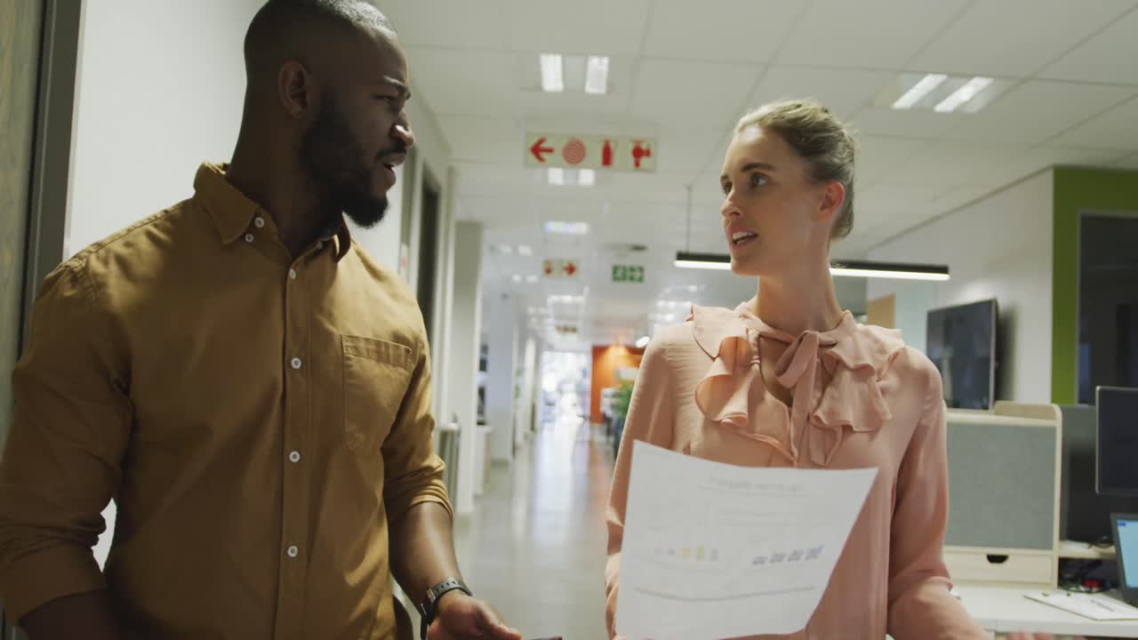 Happy diverse male and female business colleagues talking and walking in office