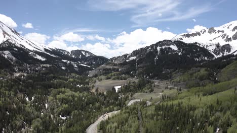 colorado rocky mountains with snowy peaks and road leading to a clearing, aerial flyover shot