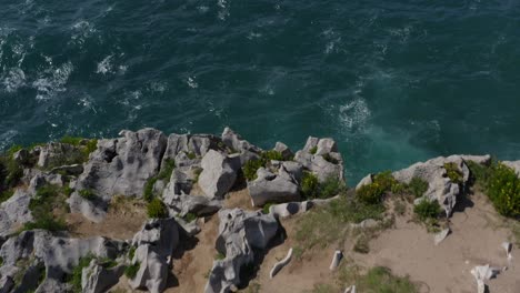 Sheer-broken-jagged-eroded-limestone-cliff-face-and-strong-waves,-tilt-down