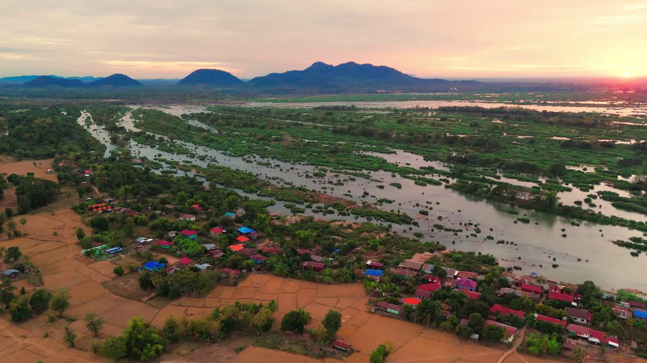 Flooded green grassland at Don Det Island, colorful houses and red sand, sunset with mountains, aerial view, copy space