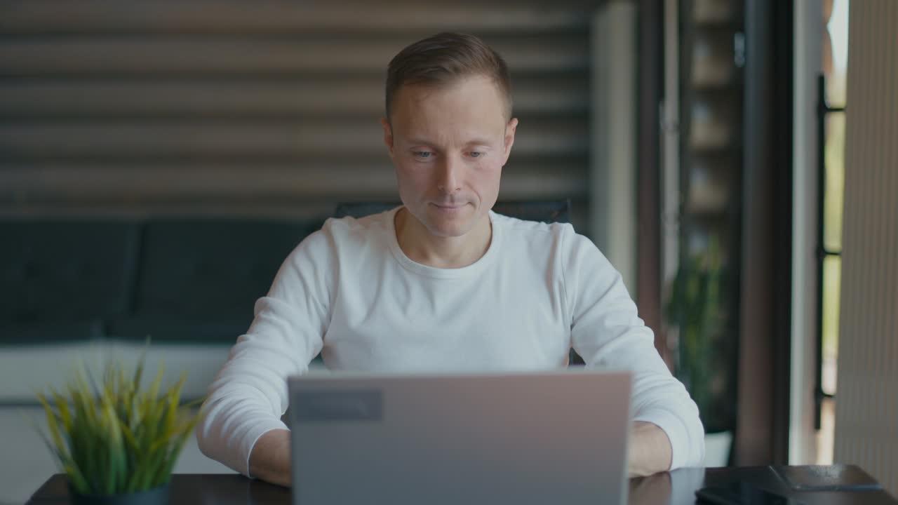Young man sitting at table with laptop is satisfied with the work done