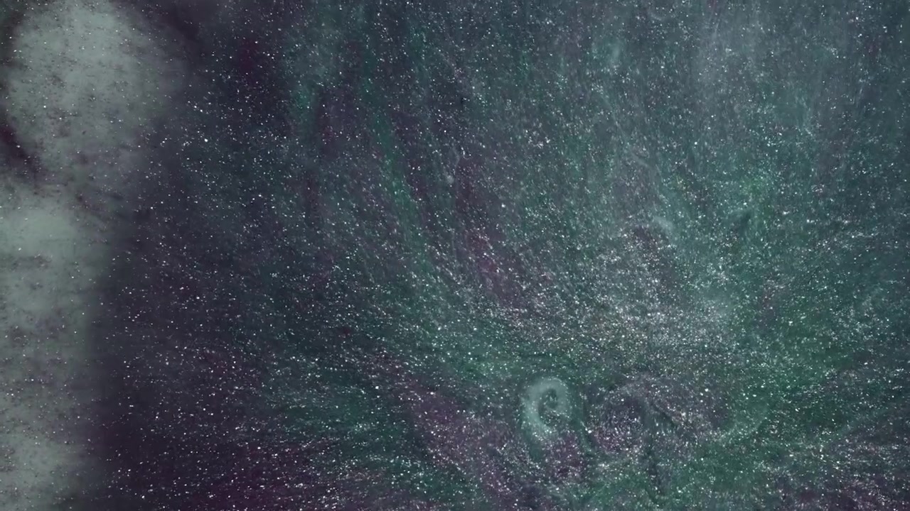 Green and purple glitter ink spreads outward in a radial pattern, creating a starfield-style abstract texture for creative backgrounds.