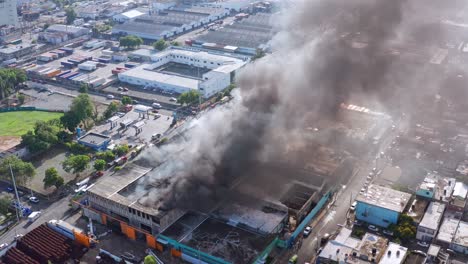 aerial view of dense column of black smoke rising from burning mattress factory on fire, santo domingo