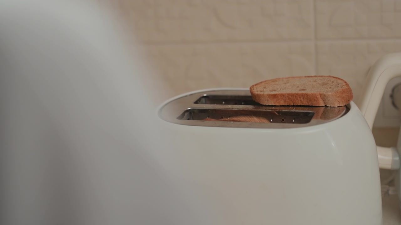 Person retrieves toast from warm toaster, ambient tune accompanies lovers morning routine, backview silhouette and gentle reach, toasted slices stacked, soft light, cozy kitchen, slow cinematic