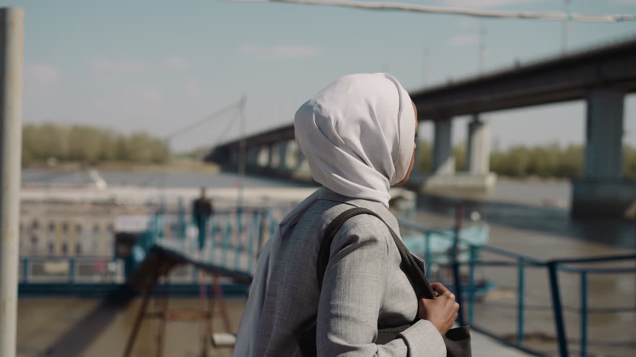 Positive Muslim woman with hijab walks along embankment