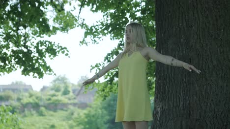 mujer con vestido amarillo bailando junto al árbol en el parque de verano