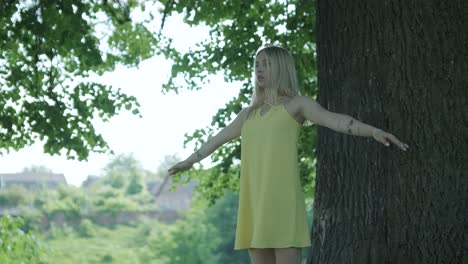 woman in yellow dress dancing by tree in summer park