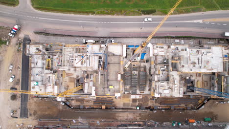 aerial top down shot of construction site with cranes and driving cars on road