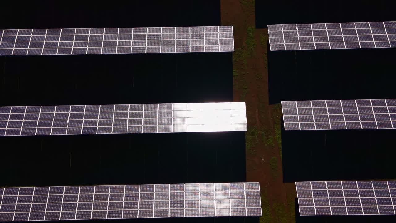 Pannelli solari sono disposti in file su un ampio campo a mezzogiorno, con la luce del sole che si riflette sulle superfici, mostrando un progetto di energia rinnovabile in funzione.