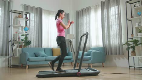 vista lateral de una mujer asiática que busca reloj inteligente y entrenamiento para caminar o correr en una cinta de correr en casa
