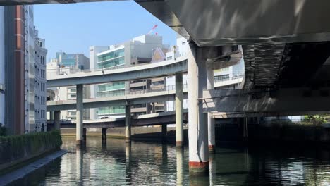 underneath a city bridge, sunlit waterway, urban architecture and reflections, clear day