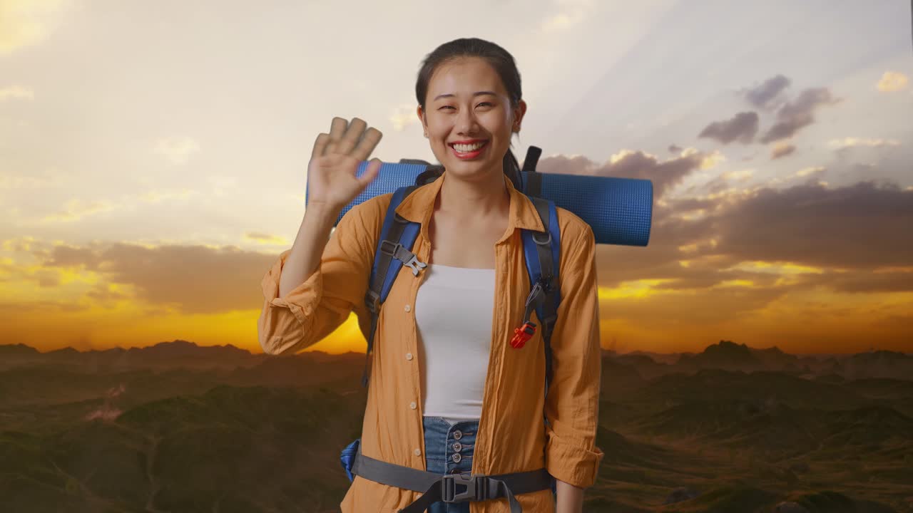 Asian Female Hiker With Mountaineering Backpack Waving Hand And Saying Bye While Standing On The Top Of Mountain During Sunset Time