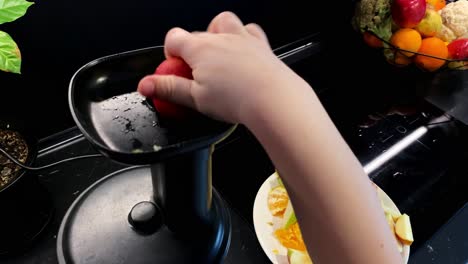 cámara lenta el niño pone trozos de manzana roja en el exprimidor de jugo, fondo negro