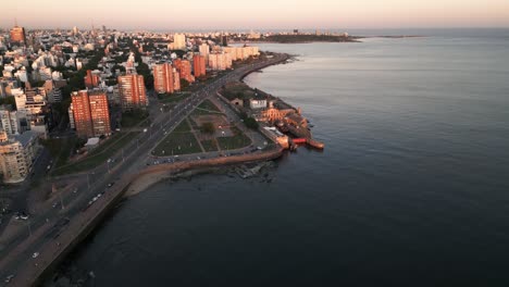 Aerial-view-descending-to-Montevideo-Gran-Bretaña-coastal-highway-road-alongside-Playa-del-Gas-sunlit-high-rise-cityscape
