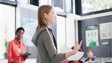 diverse female teacher and happy schoolchildren at desks reciting in school classroom