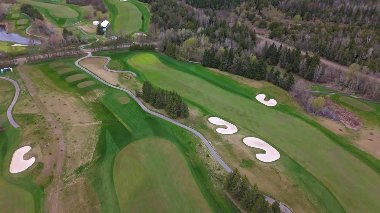 Street between green golf course and sand bunker forest landscape of Canada. Aerial top down flyover shot. Cloudy day in spring.