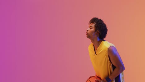 Video-of-biracial-male-basketball-player-throwing-ball-on-orange-to-pink-background