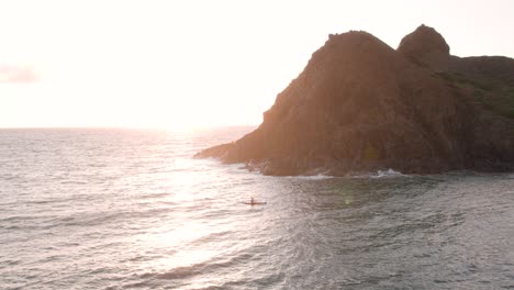 Man-kayaking-along-Moku-Nui-islet-in-Hawaii-at-sunrise,-zooming-aerial