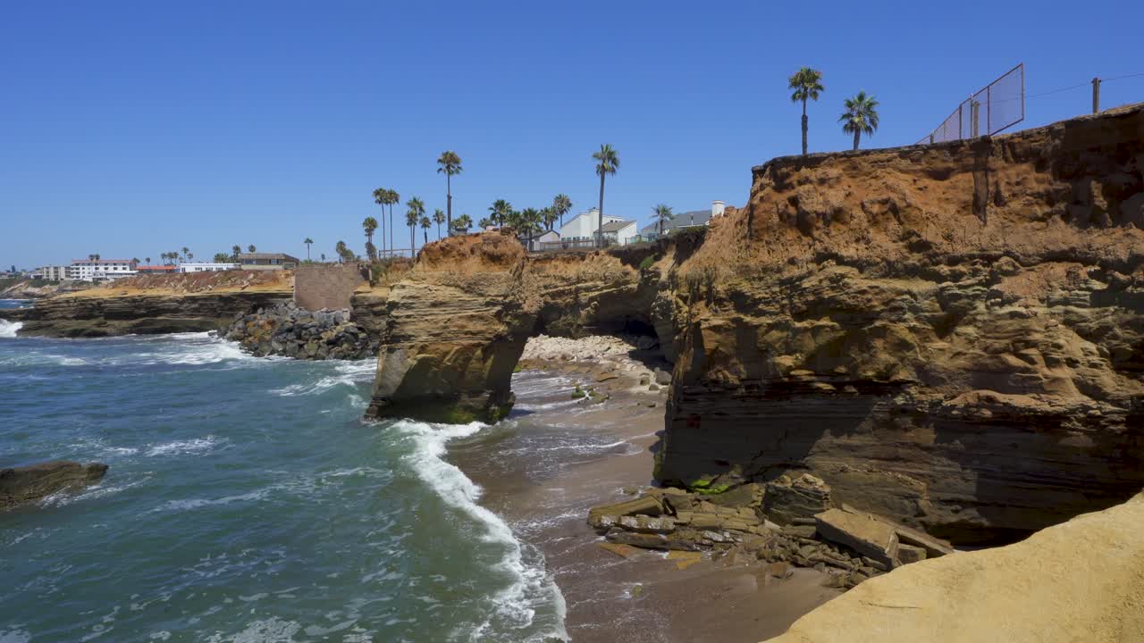 Sunset Cliffs Coastline, San Diego California, with waves crashing agains the rocks and palm trees on clear day with blue skies