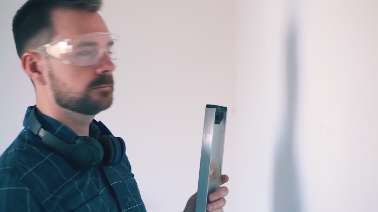 hombre cansado en camisa dibuja líneas en la pared usando el nivel en la habitación