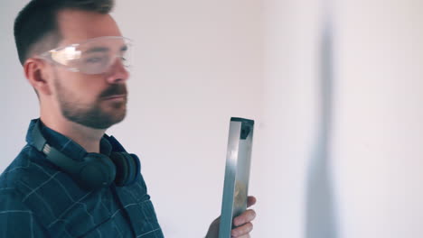 hombre cansado en camisa dibuja líneas en la pared usando el nivel en la habitación