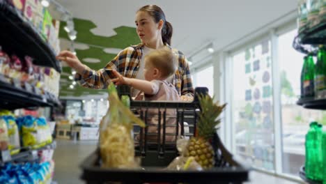 Confident-brunette-girl-in-a-plaid-shirt-together-with-her-little-daughter-makes-purchases-and-chooses-goods-in-a-supermarket-during-her-shopping