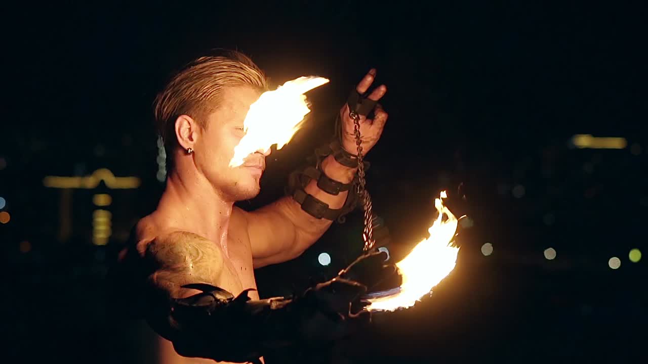 Young blond male spins two burning pois tied together Slow motion shot Close-up shot