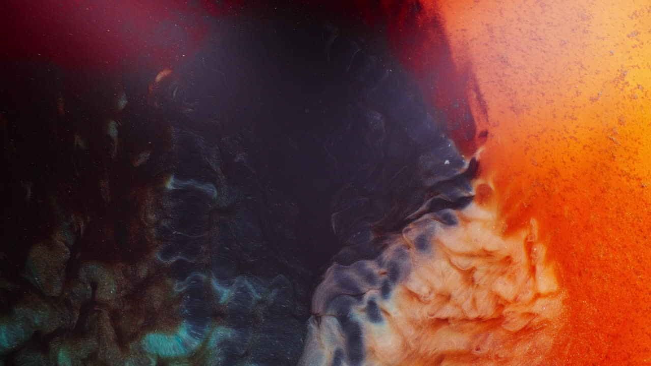 Macro shot of swirling inks forming a shimmering galaxy pattern with blue, violet, red, and orange pigments blending in motion