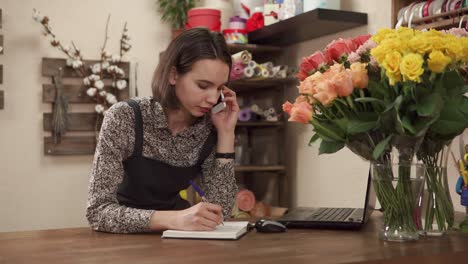 una florista hablando por teléfono y tomando notas.